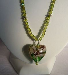 Ref: P016.     Green glass heart with a lilac flower within the glass measuring 1 inch across.  The wire has small sparkly green beads and silver plated spacers.  Length is 20 inches and has a fancy silver plated heart clasp. Handmade Green Jewelry For Valentine's Day, Green Heart-shaped Beaded Necklace Gift, Glass Heart Beads Jewelry, Handmade Heart-shaped Czech Glass Jewelry, Green Heart-shaped Beaded Necklaces, Green Glass Jewelry With Faceted Beads, Green Wire Wrapped Czech Glass Beaded Necklaces, Wire Wrapped Green Glass Jewelry, Green Wire Wrapped Glass Jewelry