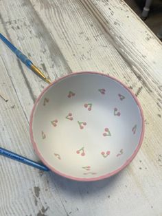 a white bowl with hearts painted on it and two blue handled spoons next to it