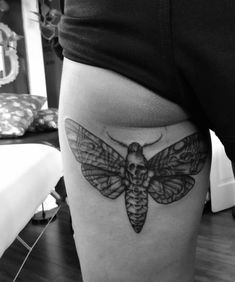 a black and white photo of a moth tattoo on the side of a woman's thigh