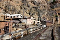 an old train track running through a mountain side town with buildings on the sides and mountains in the background