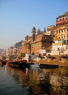 several boats are docked in the water near some buildings and people walking on the shore