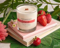 a strawberry candle sitting on top of a book next to some strawberries and flowers