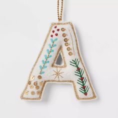 an embroidered letter ornament hanging from a gold chain