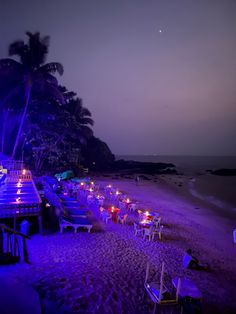 the beach is lit up at night with many tables and chairs lined up on it