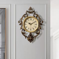 a gold clock mounted to the side of a white wall next to a mirror and door