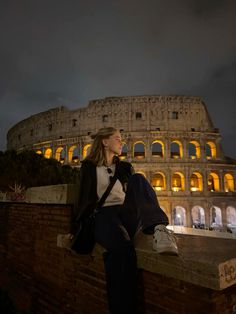 a woman sitting on top of a brick wall next to an illuminated colossion