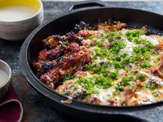 a skillet with meat and vegetables in it next to a cup of milk on a table