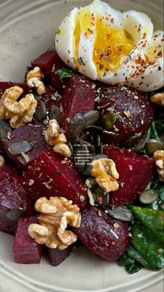 a white plate topped with beets and nuts next to an egg on top of it