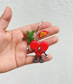 a hand holding a red heart keychain with two small green leaves on it