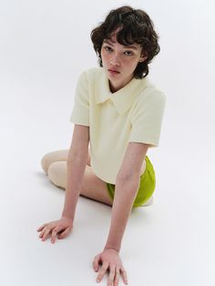 This piece of clothing is a short-sleeved knitted top with a textured pattern. It features a prominent collar with a single button fastening at the neck. The fit is snug around the waist and loose around the shoulders and chest. The sleeves end above the elbow with a soft, ribbed finish.- The garment displays a classic collar design, enhancing its structured neckline.- It has a cropped cut, sitting just above the waist, revealing the midriff slightly.- A single pearlescent button adds a subtle decorative element while serving as a functional closure at the throat. White Knit Collared Top, Spring Textured Knit Top With Collared Neckline, Spring Collared Textured Knit Top, Knit Sweater With Ribbed Collar And Short Sleeves, Short Sleeve Knit Sweater With Ribbed Collar, Fitted Knit Top With Seamless Collar And Short Sleeves, Fitted Short Sleeve Knit Top With Seamless Collar, Fitted Textured Knit Short Sleeve Sweater, Spring Textured Knit Collared Top