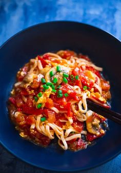 a black plate topped with noodles and vegetables next to chopsticks on a blue table