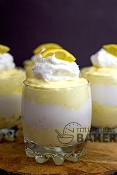 three glasses filled with lemon pudding on top of a wooden table and topped with whipped cream