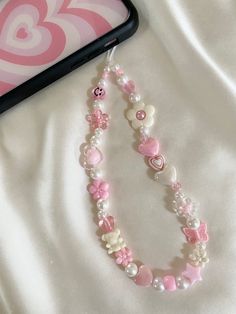 two pink and white necklaces laying on top of a bed next to a cell phone