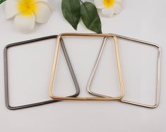 three pieces of metal sitting on top of a white surface next to flowers and leaves