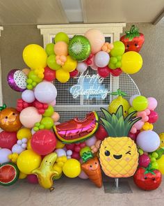 an assortment of fruit and vegetables on display in front of a building with a welcome sign