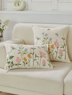 two pillows sitting on top of a white couch next to a vase filled with flowers