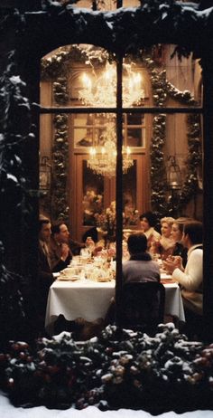 a group of people sitting at a table in front of a window with christmas decorations on it