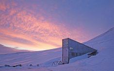 a building sitting on the side of a snow covered mountain under a pink sky with clouds