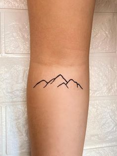 a woman's leg with a small tattoo on her left arm and mountains in the background