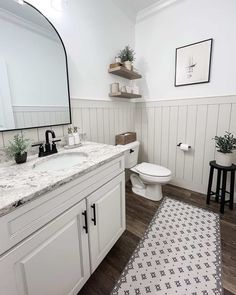 a bathroom with white walls and wood flooring is pictured in this image, there is a rug on the floor next to the sink