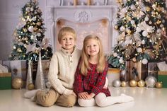 two young children sitting on the floor in front of christmas trees and presents, posing for a photo