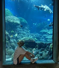 a woman is sitting in front of an aquarium looking at the fish and other animals