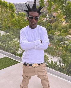 a young man with dreadlocks standing in front of a fenced area and looking at the camera