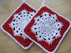 two red and white crocheted squares sitting on top of a wooden table