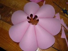 a pink flower made out of foam sitting on top of a wooden table next to scissors and tape