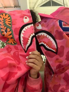 a girl in pink camo hoodie holding up a shark mask