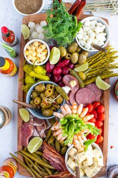 an assortment of meats and vegetables on a wooden platter with olives, tomatoes, peppers, asparagus