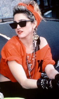 a woman in an orange shirt and black gloves sitting on a bench with her hand resting on the arm