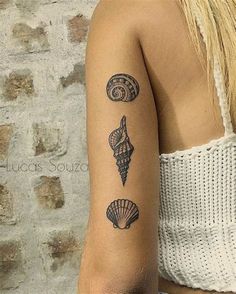 a woman's arm with tattoos on it and seashells in the background