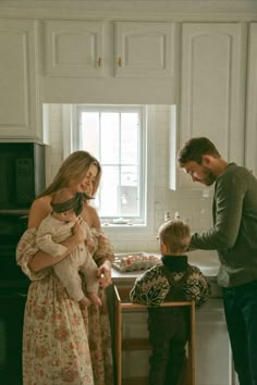 a man standing next to a woman holding a baby in front of a stove top oven