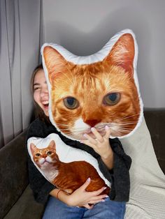 a woman sitting on a couch holding an orange and white cat pillow over her face