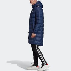 a man in a blue down jacket and black pants standing on a white background wearing adidas shoes