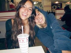 two women sitting at a table with drinks in front of them and smiling for the camera