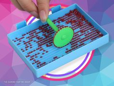 a person using a green plastic scooper to scoop red beads into a blue container