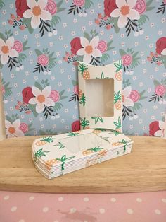 a stack of folded papers sitting on top of a wooden table next to a flowered wallpaper