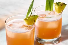 two glasses filled with drinks sitting on top of a white table next to each other