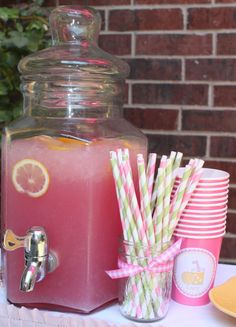 a beverage dispenser filled with pink lemonade and straws on a table