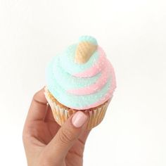 a hand holding a cupcake with frosting and an ice cream cone on top