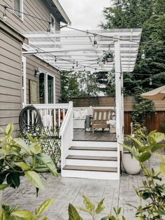 an outdoor patio area with white furniture and wooden steps leading up to a deck that is surrounded by greenery