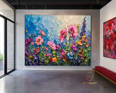 an abstract floral painting hangs on the wall next to a red bench in front of a large window