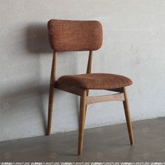 a wooden chair against a white wall with a brown seat cover on it's back