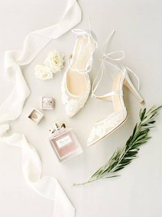 wedding shoes, perfume and flowers laid out on a white surface