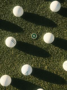 several white golf balls on the grass with one green marker in the middle and four black ones behind them