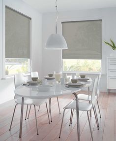 a white dining room table and chairs with blinds on the windows behind them, in front of an open window