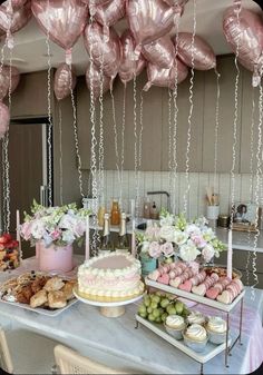 a table topped with lots of pink balloons and desserts next to a counter filled with food