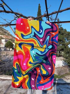 a person holding up a colorful blanket in front of a blue sky and some trees